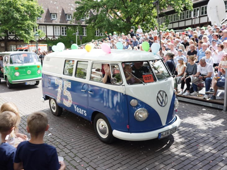 Zwei Autos in einem Festzug. Im Hintergrund Menschen auf einer Tribüne.