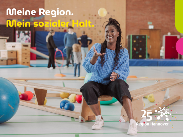 Eine Frau sitzt in der Turnhalle beim Kinderturnen und fängt einen Ball.