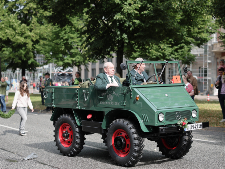 Zwei Männer in einem offenen Wagen bei einem Festumzug.