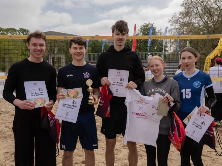 Drei Jungs und zwei Mädchen stehen nebeneinander und lachen in die Kamera. Ein Junge hält einen goldenen Pokal in der Hand.