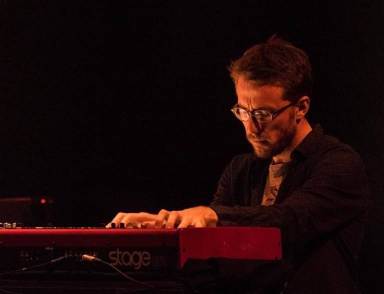 Mann mit mit kurzem Haar, Bart und Brille an einem Keyboard