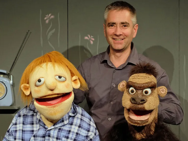 Mann mit zwei großen Handpuppen, eine ist ein rothaariger Junge, die andere ein Affe