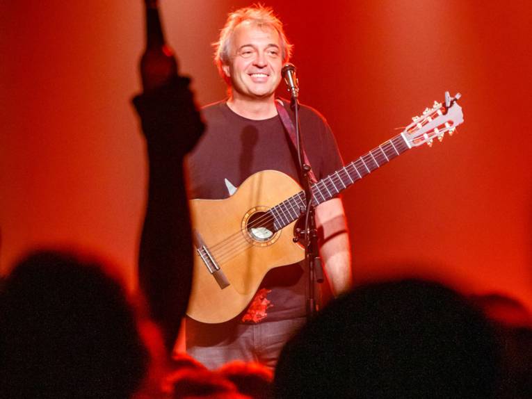 Mann mit Gitarre sitzt auf einer Bühne in rotem Scheinwerferlicht.