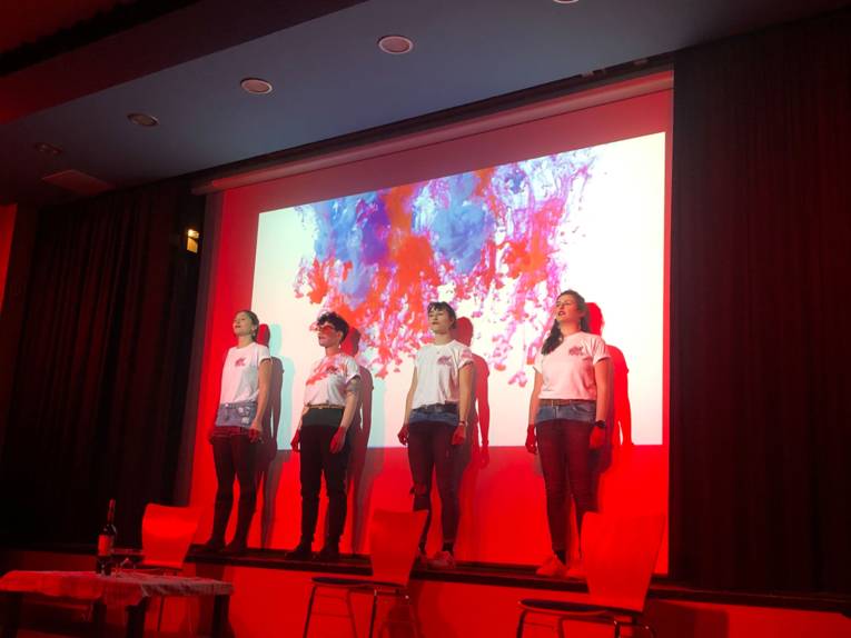 Vier Frauen stehen auf einer rot beleuchteten Bühne