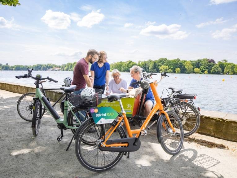 Menschen sitzen mit Fahrrädern am Ufer des Maschsees