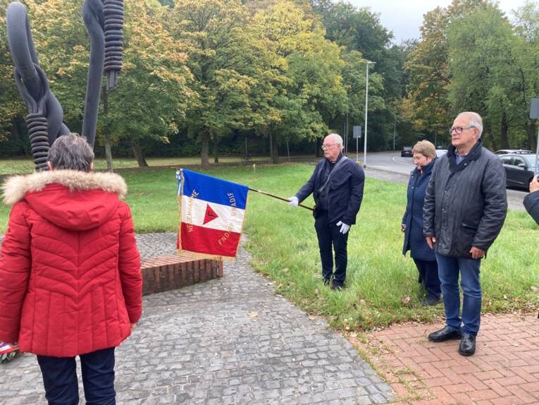 Ein Standartentr&auml;ger und weitere Besuchenden vor dem Mahnmal
