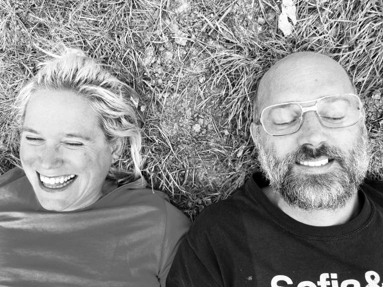 Eine Frau und ein Mann liegen auf einer Wiese, beide lachen.