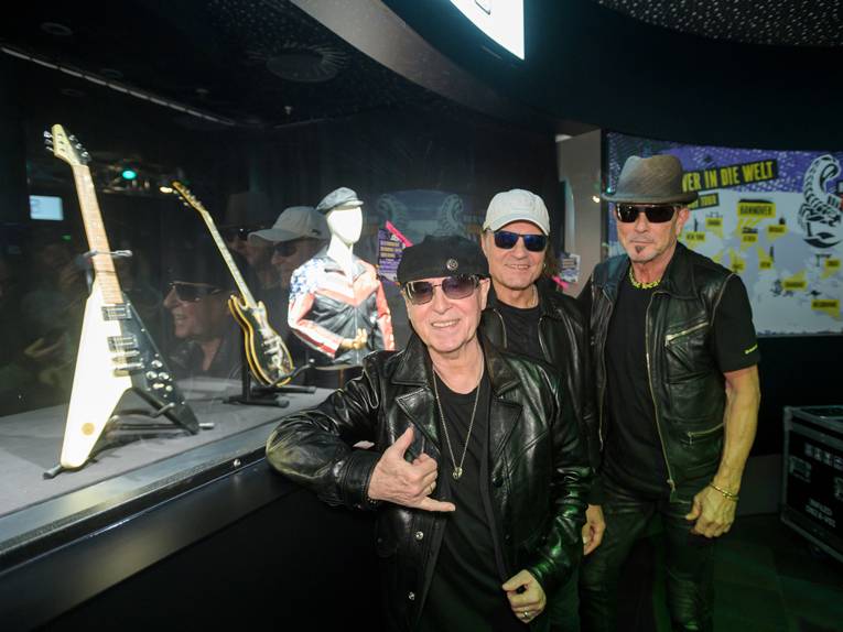 Drei Männer vor einem Glaskasten mit Gitarren