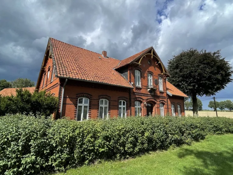Rotes Backsteingeb&auml;ude hinter einer Hecke