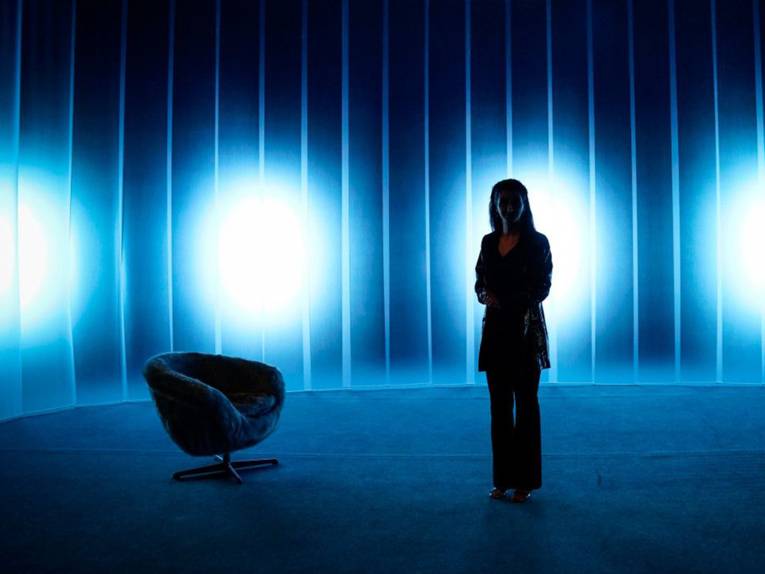 Die Schauspielerin Şafak Şengül auf einer dunklen Bühne, auf der ein Sessel steht.