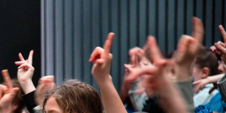 Kinder heben ihre Arme und Finger und signalisieren dadurch, dass sie etwas beitragen oder eine Frage stellen wollen.