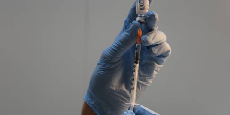 Hände in blauen Handschuhen ziehen ein Impfdosis in eine Spritze