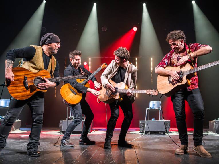 Vier Männer mit Gitarren auf einer Bühne.