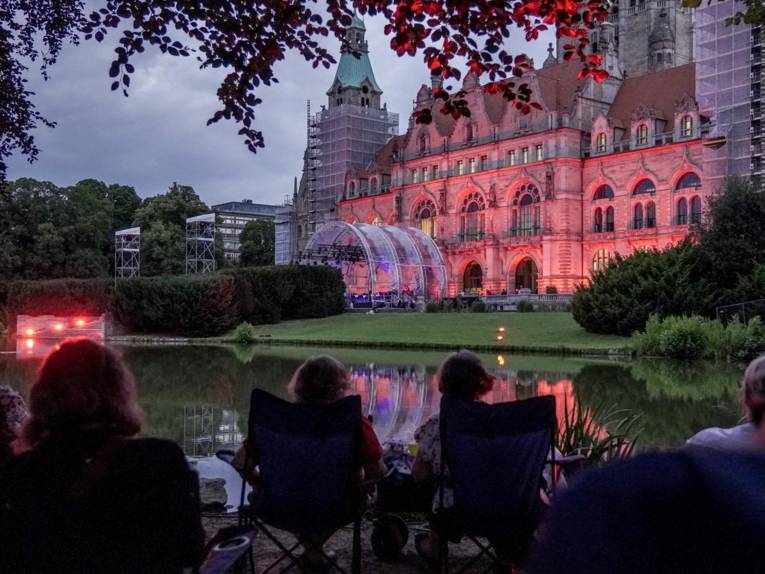 Menschen in einem Park. Im Hintergrund eine beleuchtete Bühne.