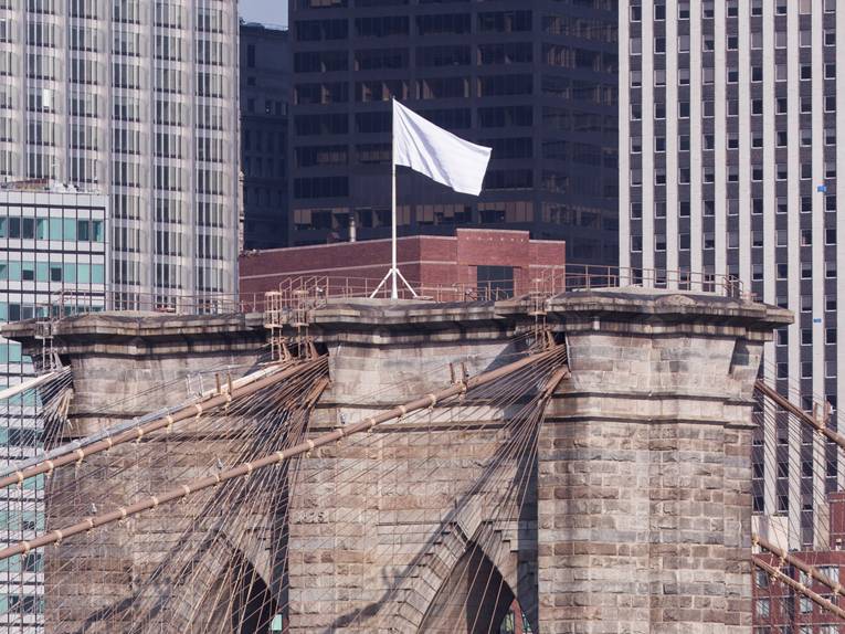 das Bild zeigt einen der Köpfe der Brooklyn Bridge, auf dem eine weiße Fahne weht