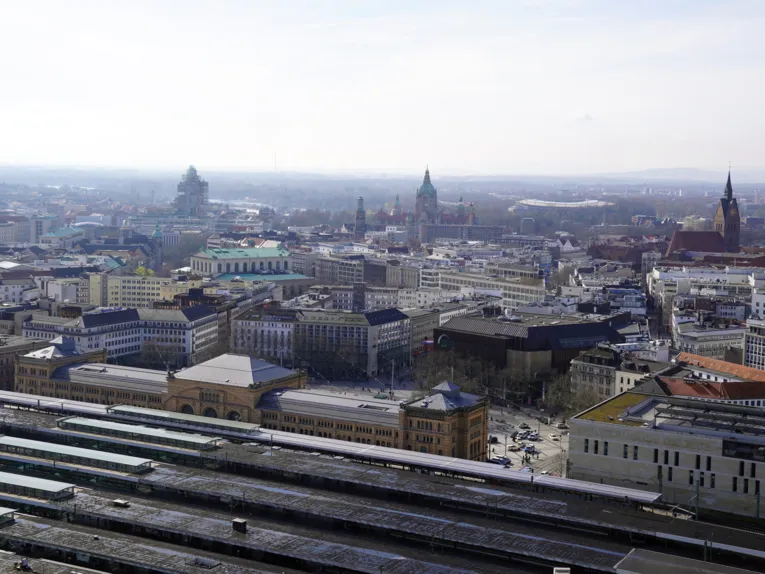 Blick aus der Vogelperspektive auf eine Stadt, vorn Gleise, Bahnsteige und ein breites Gebäude