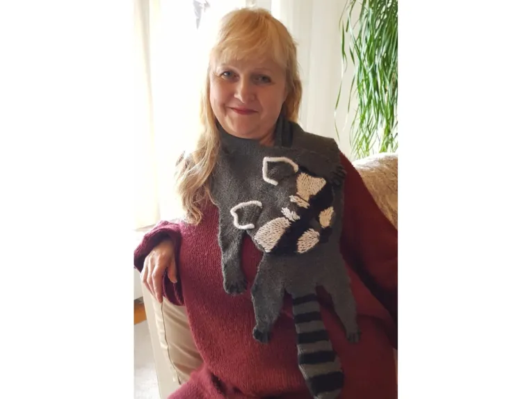 Eine Frau in einem Strickpulli mit einem Strickschal in Form eines Wachbären.