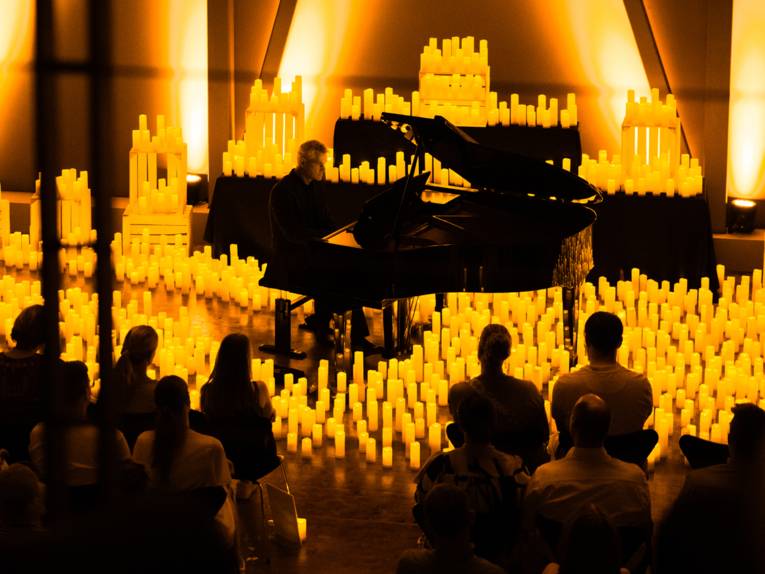 Ein Pianospieler ist von einer Vielzahl von Kerzen umgeben und spielt vor Publikum.