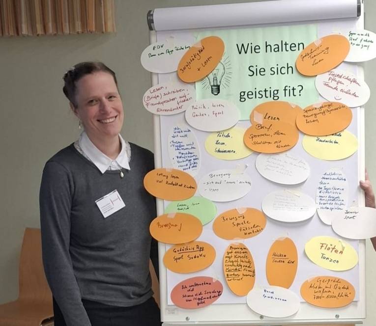 Eine junge Frau steht neben einem Plakat. Darauf steht "Wie halten Sie sich geistig fit" und viele Notizen dazu.