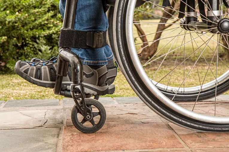 Eine Person sitzt im Rollstuhl. Zusehen sind die Füße der Person und die Reifen des Rollstuhls.