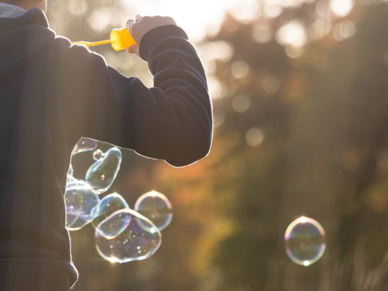 Blick von hinten auf ein Kind, das Seifenblasen pustet.
