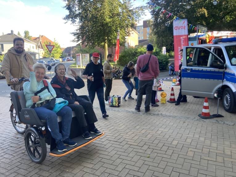 Einer f&auml;hrt Rikscha, zwei Frauen winken und fahren mit