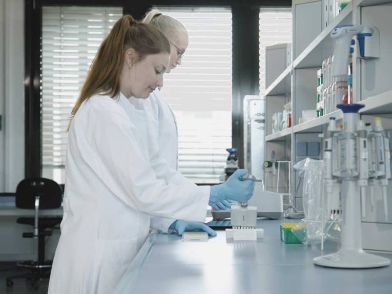 Zwei Männer und zwei Frauen in weißen Kittel gehen einen Gang entlang.