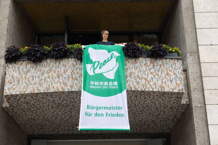 Bürgermeisterin Dr. Alexandra Sußmann hängt die Mayors for Peace Flagge auf.