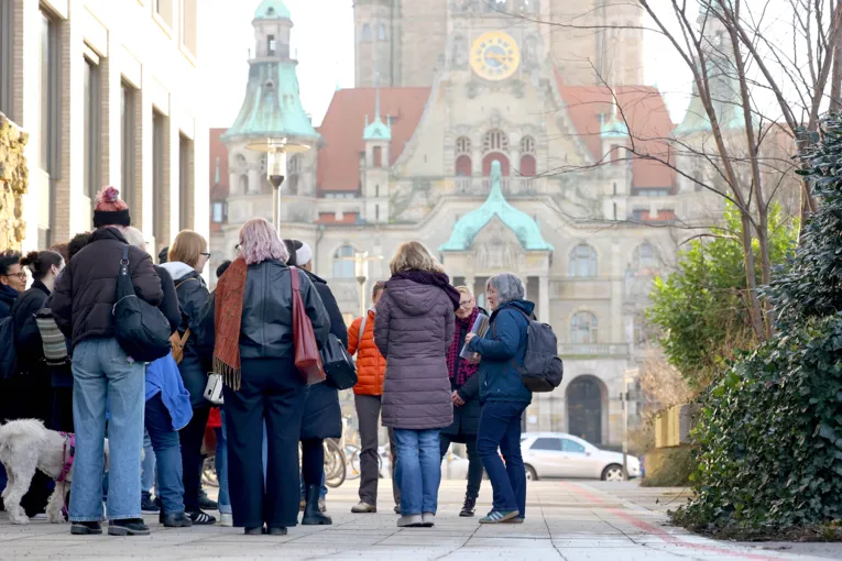 Personengruppe bei einem historischen Stadtspaziergang mit einer vortragenden Person vor dem ZeitZentrum Zivilcourage mit dem Neuen Rathaus im Hintergrund