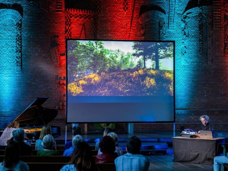 Publikum blickt in der Martinskirche auf eine Bühne mit audiovisueller Performance, einem Flügel und einem Mischpult.