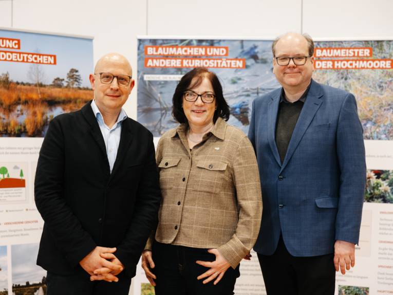 Drei Personen vor Plakatwänden