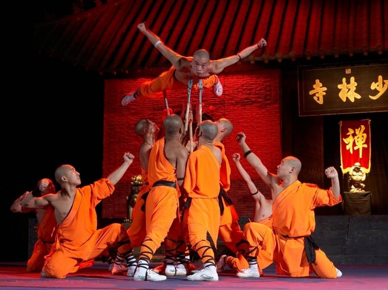 Zu sehen sind akrobatische Mönche auf einer Bühne.