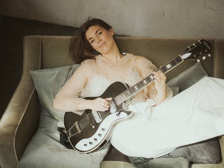 Eine junge Frau liegt mit Gitarre auf einem Sofa