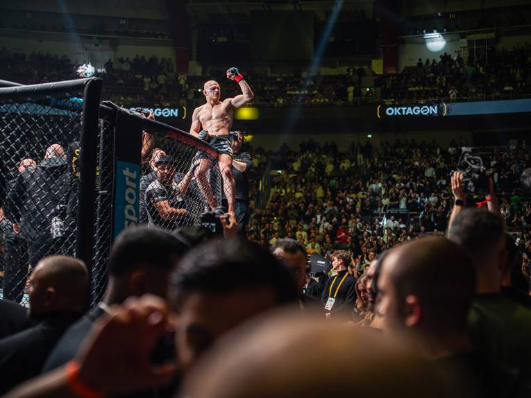 Ein MMA-Kämpfer sitzt auf der oberen Rahmenstange eines Oktagon-Ringes.