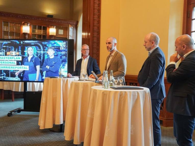 Vier Männer in einer Amtsstube. Rechts von ihnen ein Bildschirm.