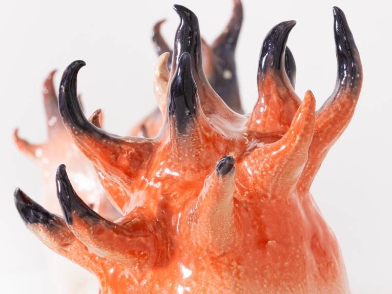 Zu sehen ist eine Keramikskulptur, aus der spitze Formen austreten, die an Hörner oder Flammen erinnern.