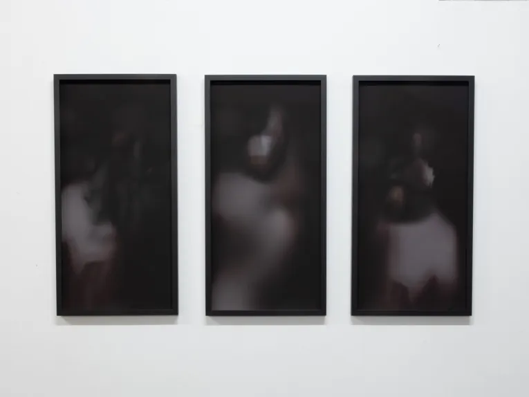 Zu sehen ist eine Arbeit von Jessika Dirks: Drei senkrechte Rechtecke verschwommene dunkle Bilder, die eine Frauenfigur andeuten.