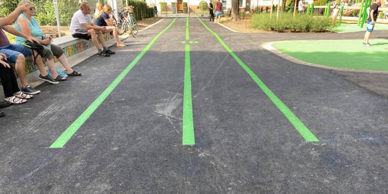 Eine Rennbahn auf einem Spielplatz. Am Rand sitzen Leute.