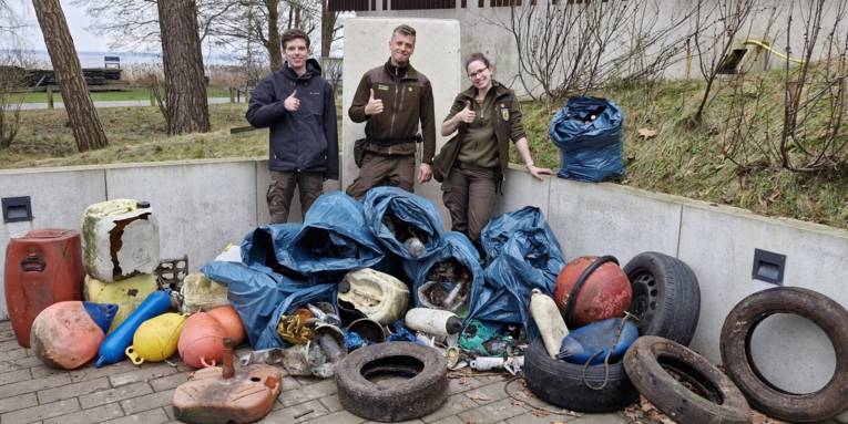 Drei Personen stehen hinter einem Haufen aus M&uuml;ll und reckten jeweils einen Daumen vor der Brust nach oben.