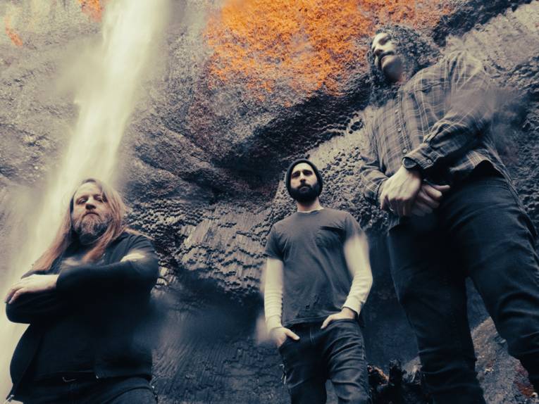 Die drei Musiker der Band vor einer Felswand.