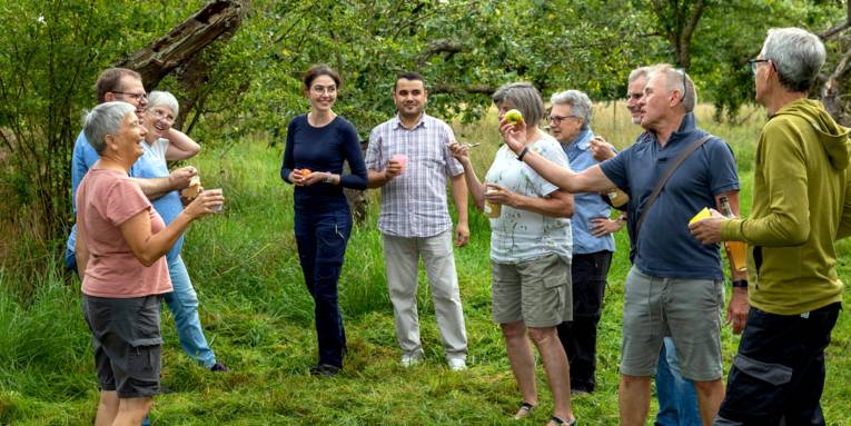 Personen stehen mit Apfelprodukten auf einer Wiese.