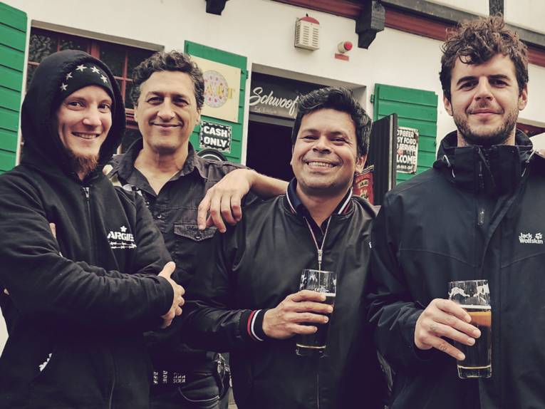 Die vier Musiker der Band mit Biergläsern vor einem Pub.