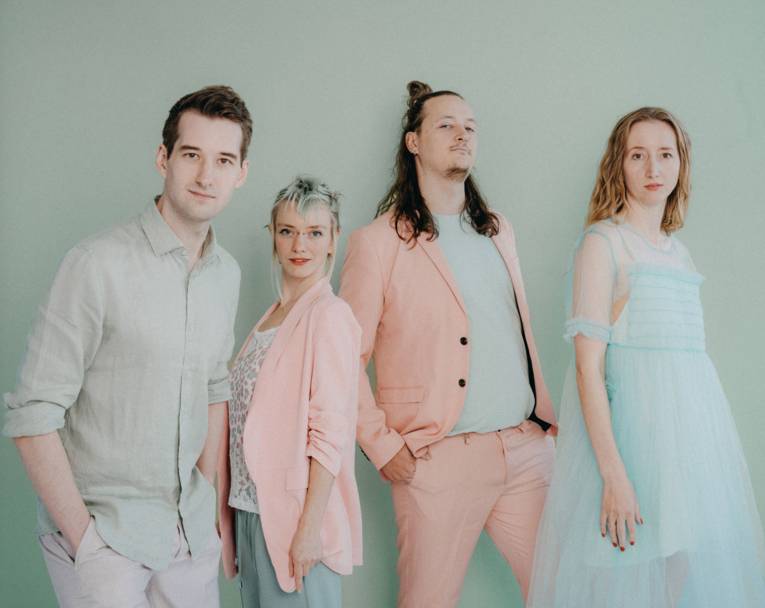 Zwei Frauen und zwei Männer in pastellfarbener Kleidung