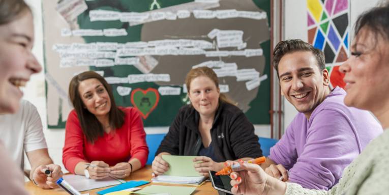 Personen sitzen an einem Tisch und beschriften Moderationskärtchen.