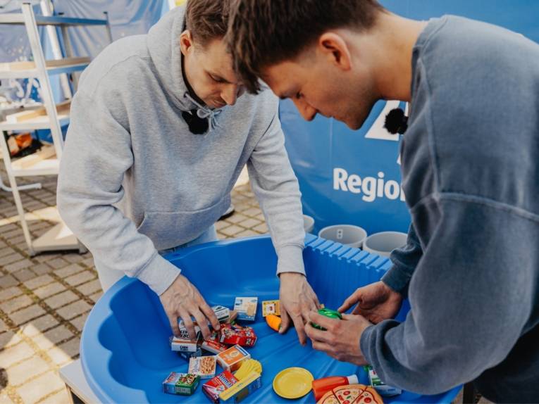 Zwei Männer kramen in einer blauen Kiste in der verschiedene Gegenstände liegen.