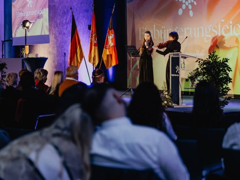 Blick über das Publikum auf die Bühne, wo feierlich Geigenmusik gespielt wird.