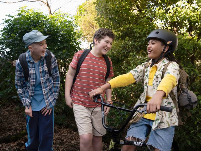 Drei lachende Jungen - einer sitzt auf einem Fahrrad