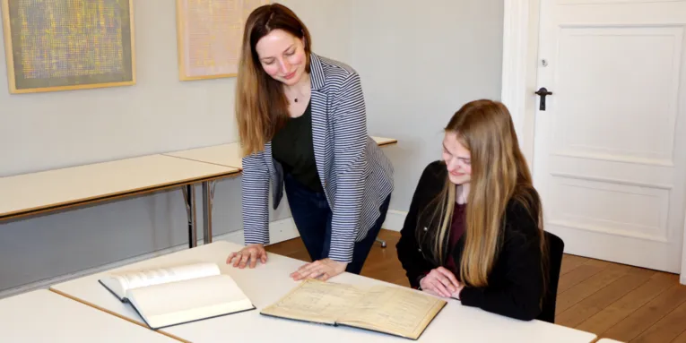 Zwei Frauen sichten historische Bücher an einem Tisch.