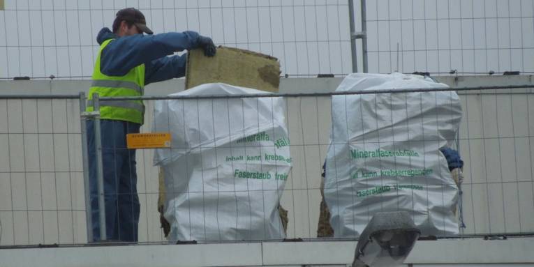Arbeiter, der Abfälle aus künstlichen Mineralfasern in speziellen Abfallsäcken mit Warnaufschrift entsorgt