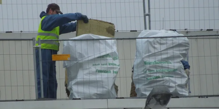 Arbeiter, der Abfälle aus künstlichen Mineralfasern in speziellen Abfallsäcken mit Warnaufschrift entsorgt